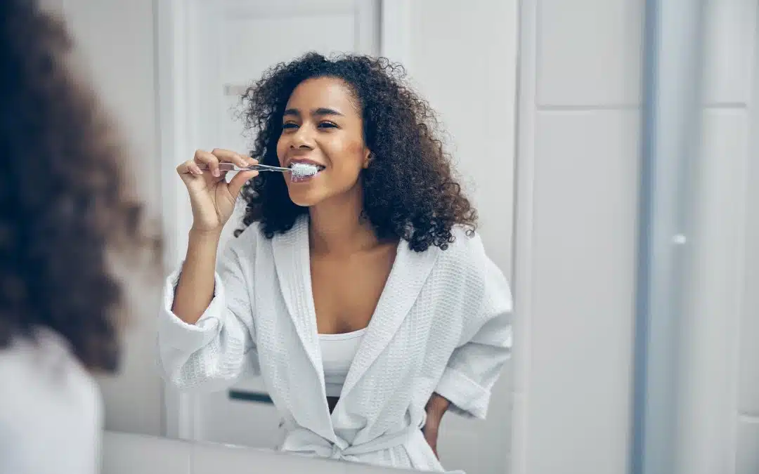 woman brushing teeth smiling in mirror - Trail West